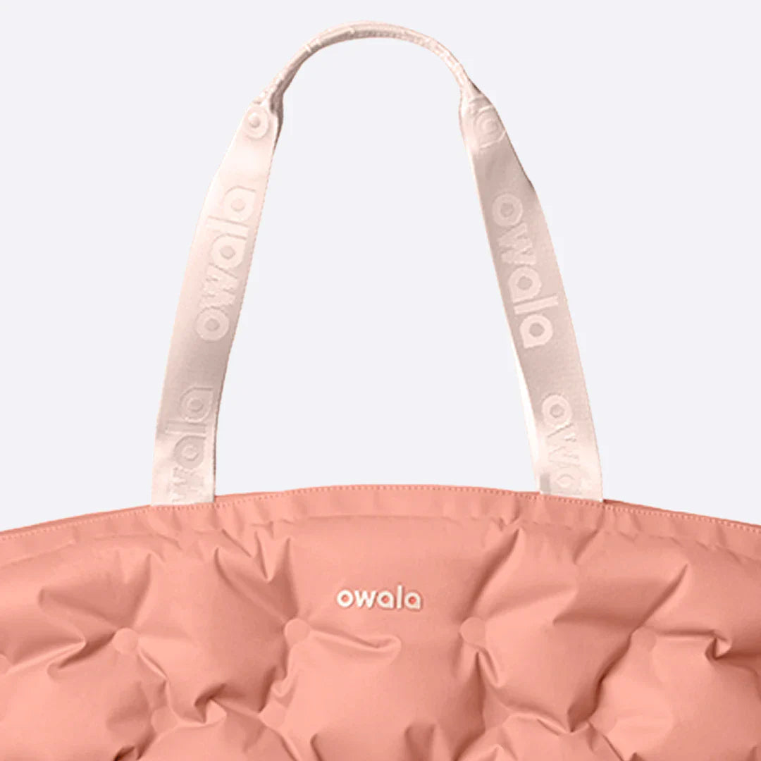 Close-up of the Owala Cloud tote in Rosewood, coral pink puffer-quilted body with blush owala-tape handles featuring repeating Owala logo and Owala logo on the body