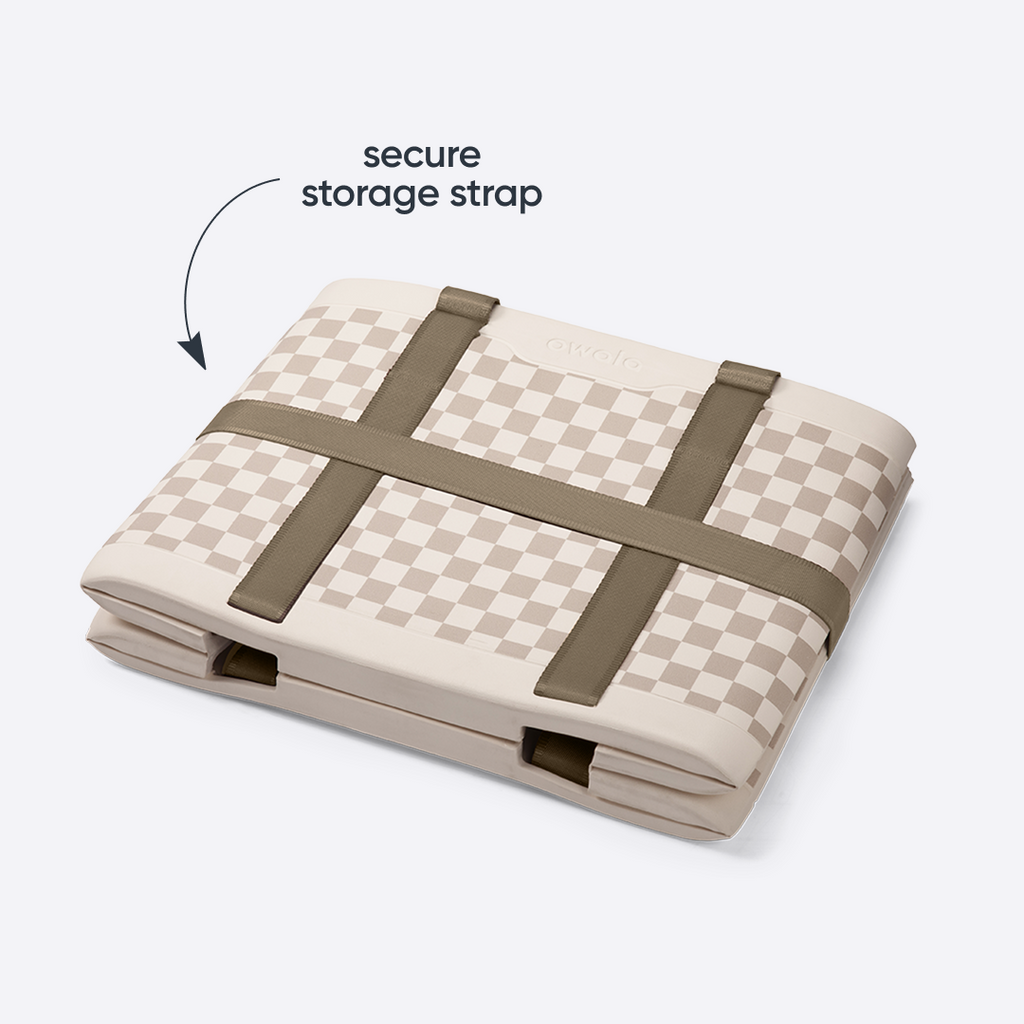 Owala Sun-Day Collapsible Tote in Checkin' In shown folded flat with its storage strap secured across the top, cream and tan checker exterior with olive green storage strap, with text overlay reading "storage strap"