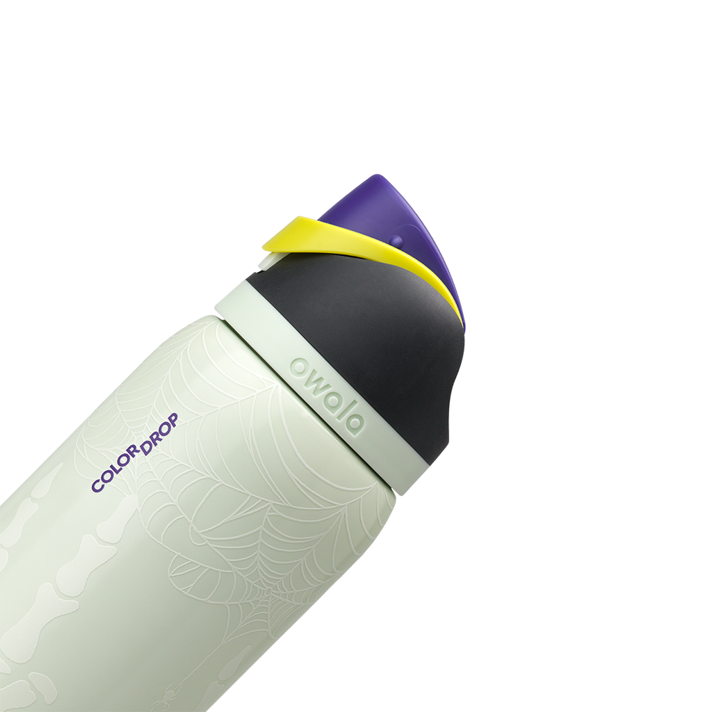 Owala FreeSip 32oz in RIP, pale mint insulated stainless steel body with "COLOR DROP" print and skeleton glow detail, flip cap closed with black lid, purple flip cap and yellow carry loop; glows in the dark