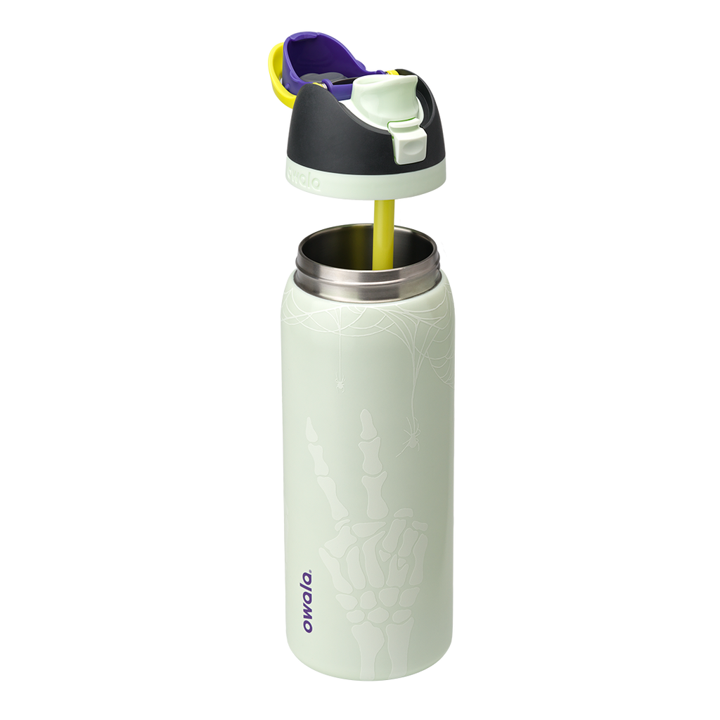 Owala FreeSip 32oz in RIP, pale mint green insulated stainless steel bottle with white skeleton-hand pattern body, dark charcoal lid, yellow carry loop, purple flip cap accent, and pale green accent ring, lid exploded; glows in the dark