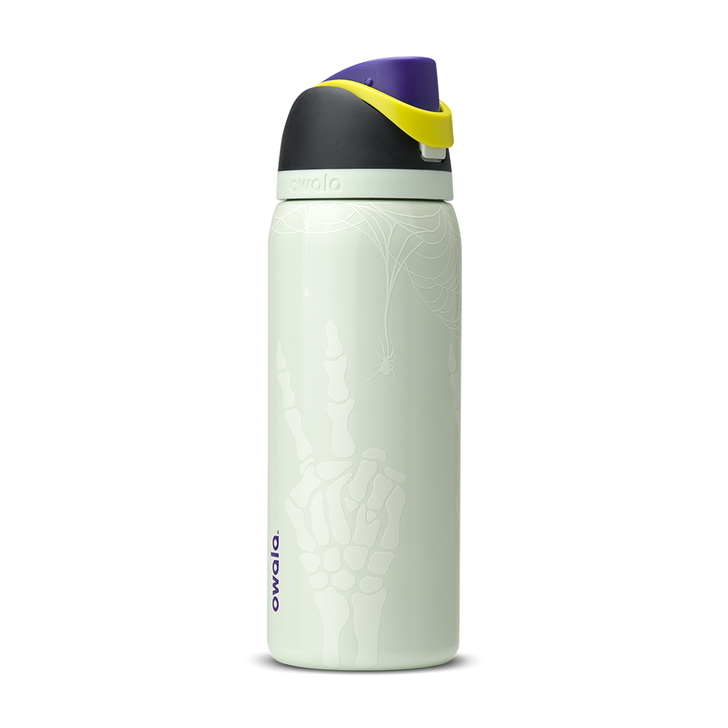 Owala FreeSip 32oz in RIP, pale mint green insulated stainless steel bottle with white skeleton-hand pattern body, dark charcoal lid, yellow carry loop, purple flip cap, and pale green accent ring; glows in the dark