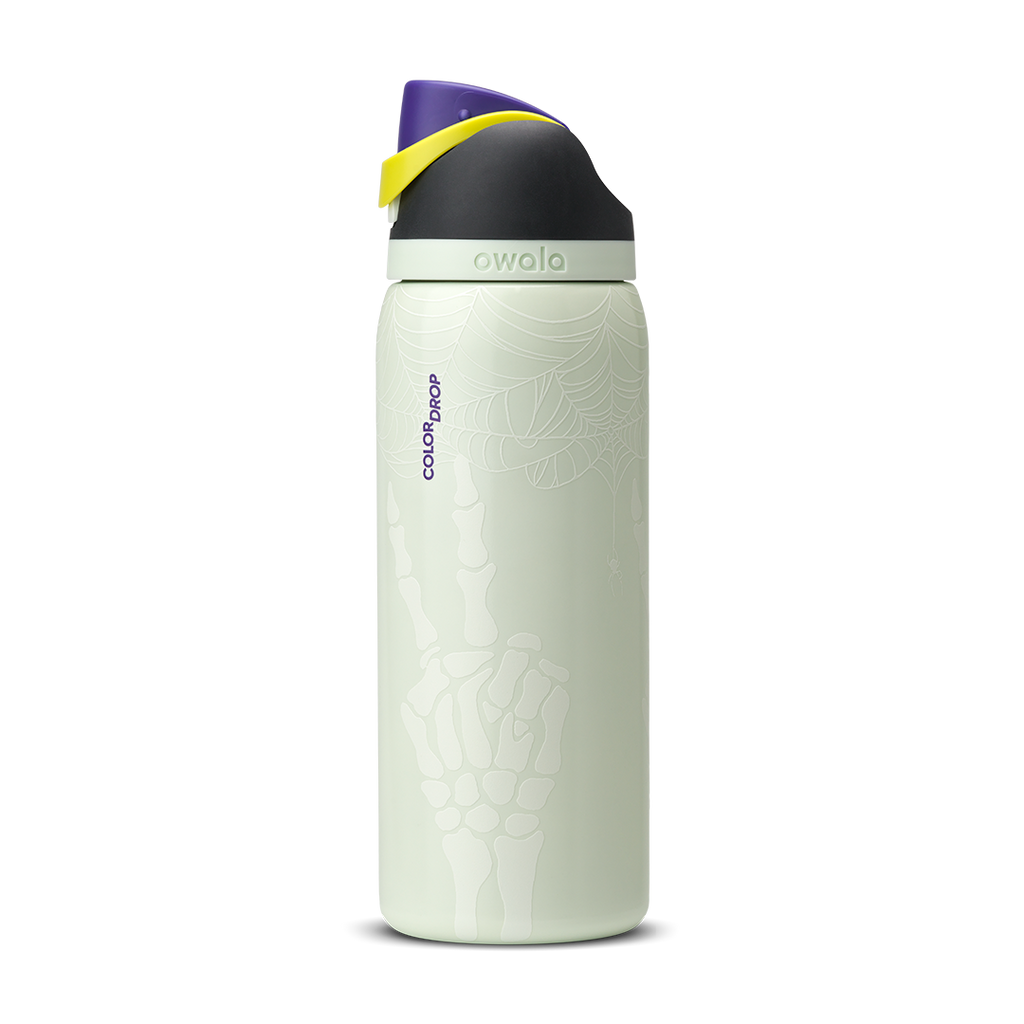 Owala FreeSip 32oz in RIP, pale mint green insulated stainless steel bottle with white skeleton-hand pattern body, dark charcoal lid, yellow carry loop, and purple flip cap, Color Drop branding on body; glows in the dark